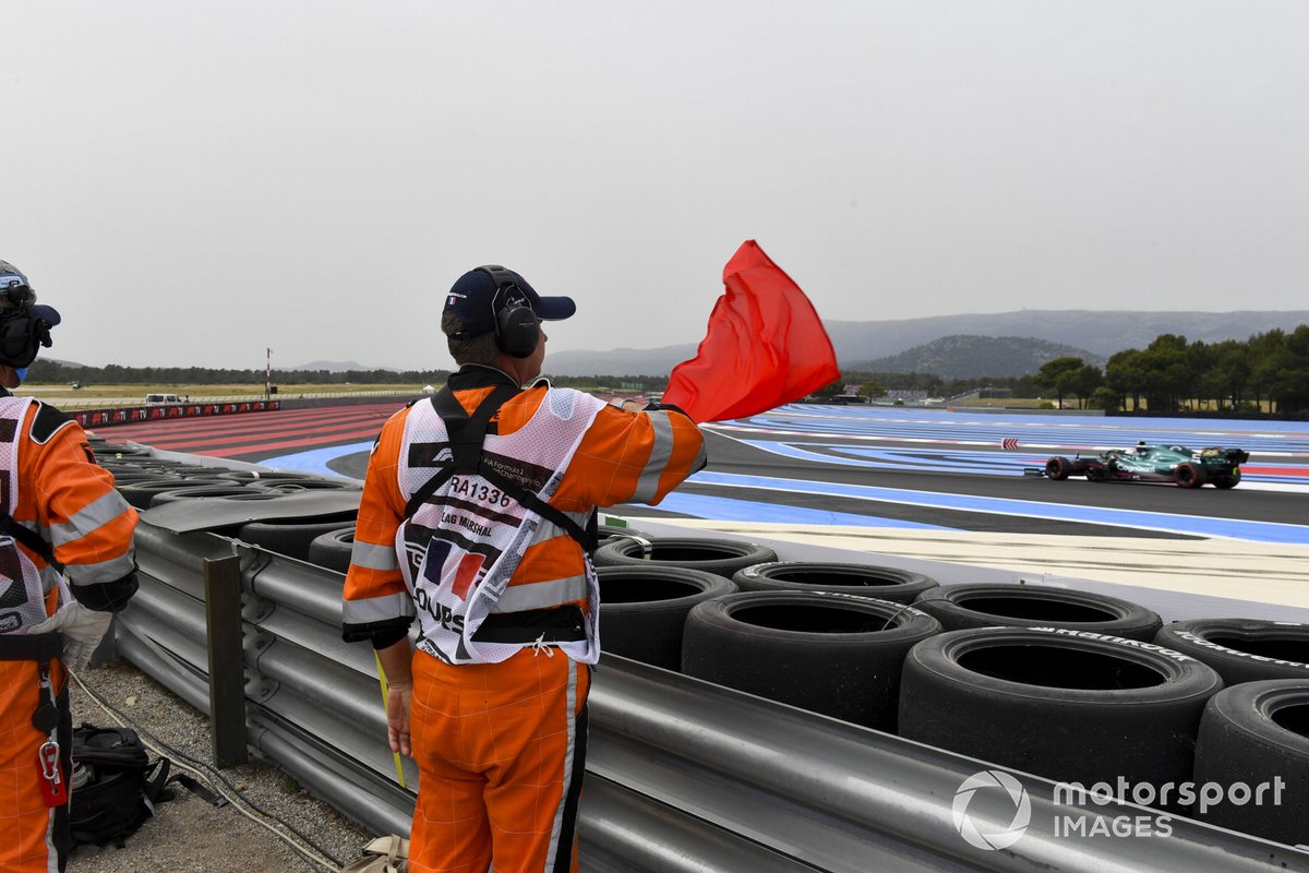 A marshal waves a red flag as Sebastian Vettel, Aston Martin AMR21, passes