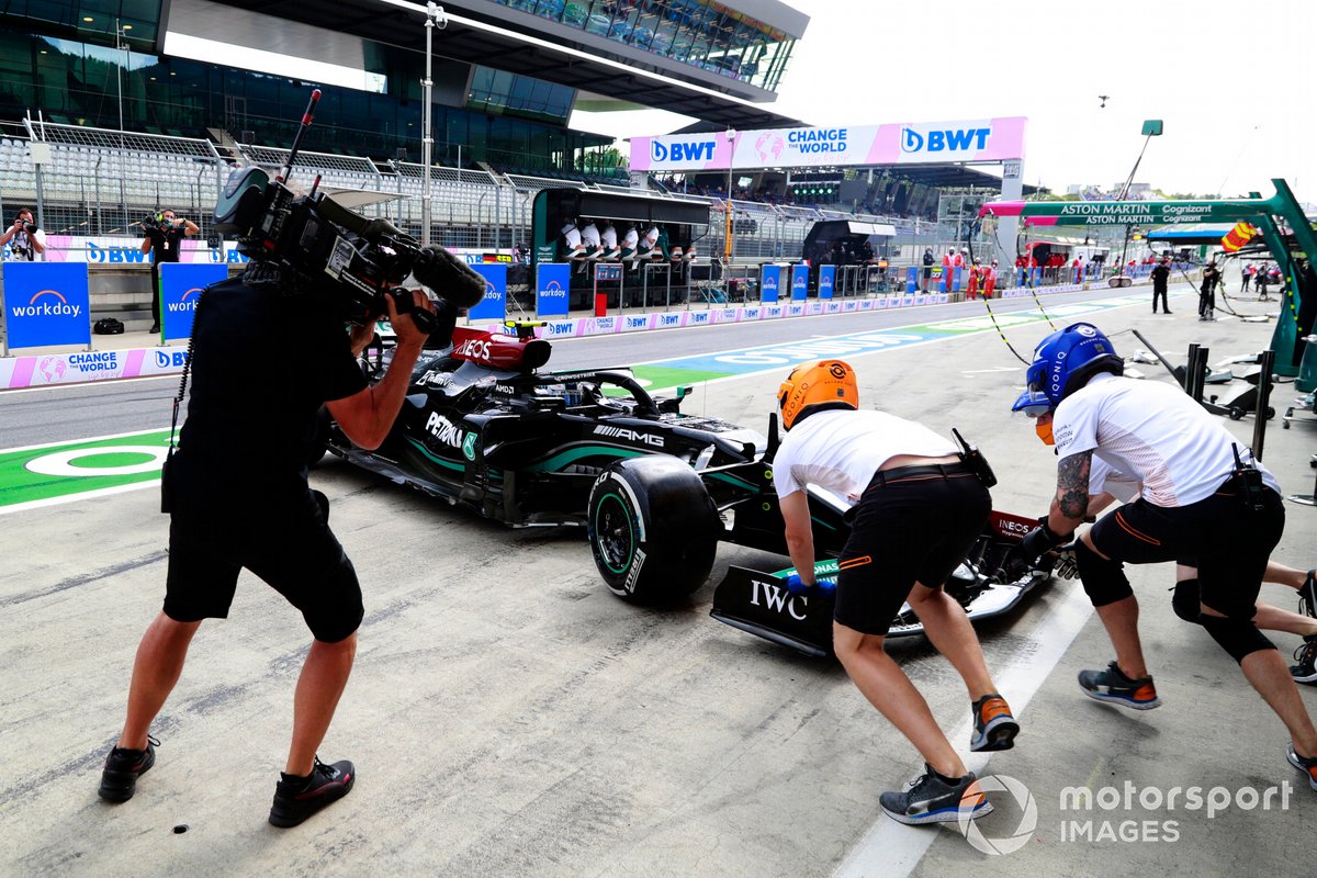 McLaren pit crew members attempt to assist Valtteri Bottas, Mercedes W12, in the pit lane
