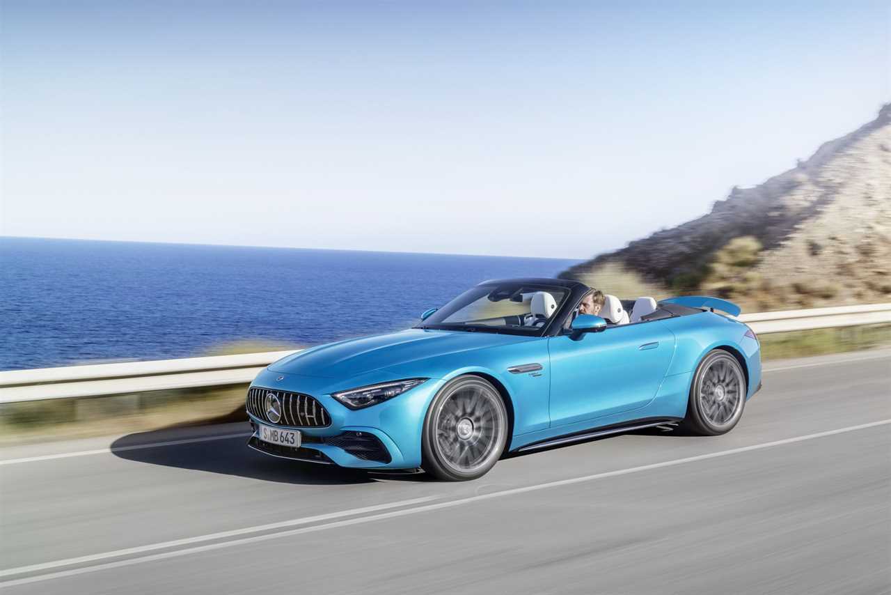 The rear 3/4 view of a blue 2023 Mercedes-AMG SL 43 driving down a mountain next to a body of water