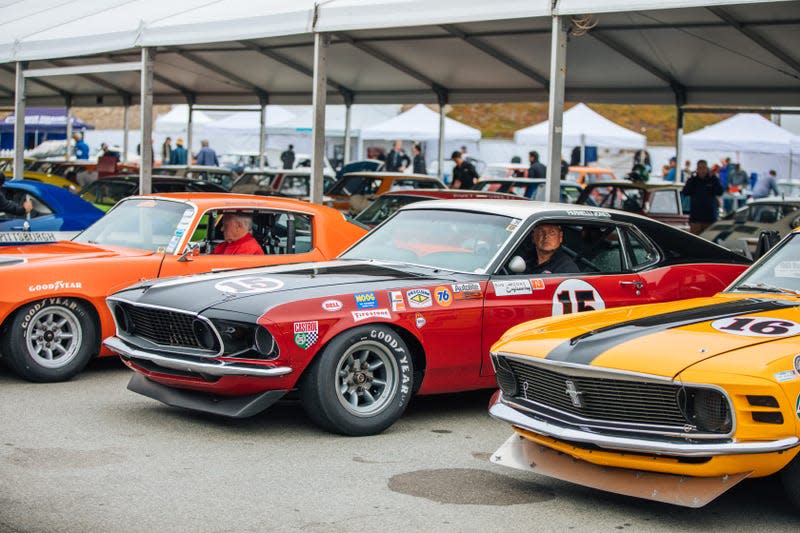 Three vintage Trans-Am race cars are parked in the paddock at Laguna Seca.